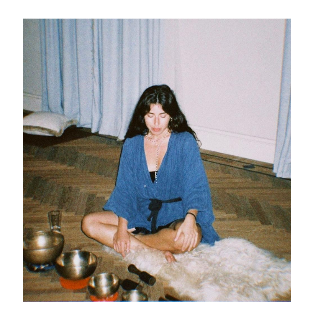 Goni seated in ceremony with singing bowls, wearing a blue dress